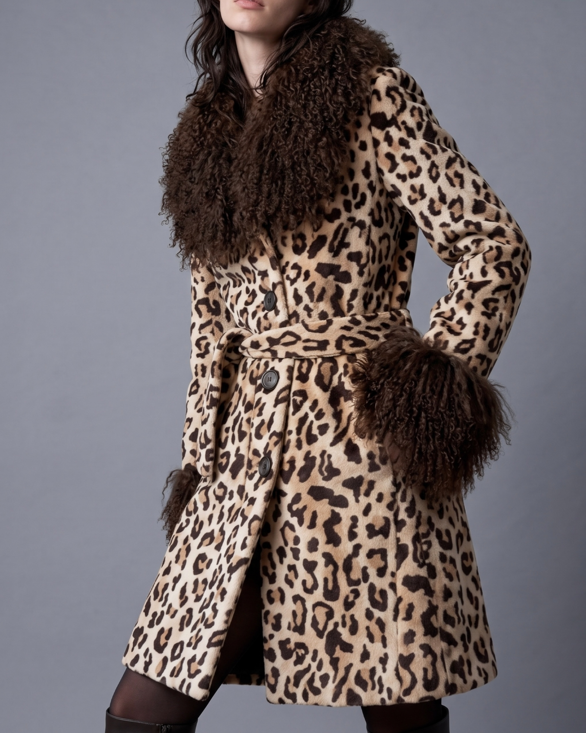 Leopard print mid length penny lane coat with dark brown shaggy curly Mongolian fur collar and cuffs shown on model walking against grey background .