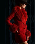 A model wearing a vibrant vintage red textured tapestry jacket and red suede skirt, jacket adorned with fluffy red Mongolian fur trim at the collar and cuffs, styled with a black wide-brim hat against a dark city closed shop gate background.